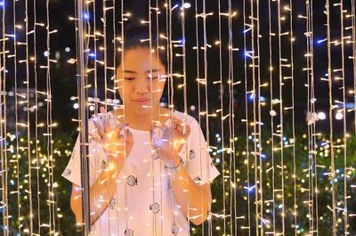 Woman looking at illuminated string lights during night