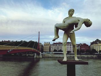 Statue by river against sky in city