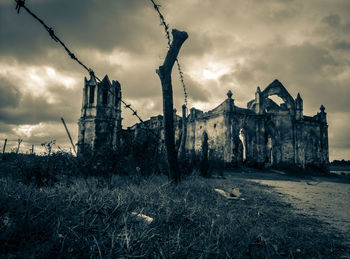 Low angle view of old ruin on field against cloudy sky