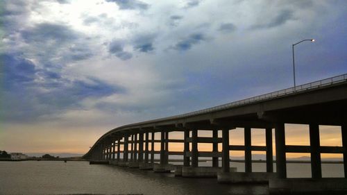 Bridge over calm sea against cloudy sky