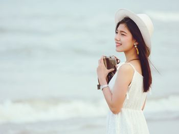 Smiling woman with camera standing at beach