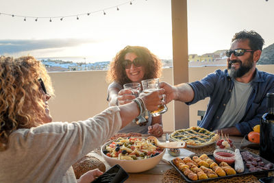 Friends toasting beer glasses at table in terrace during sunset