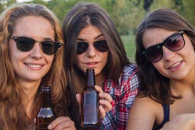 Portrait of young women drinking alcohol while sitting on field