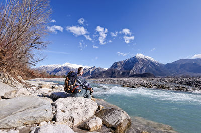 Man sitting on rock against sky