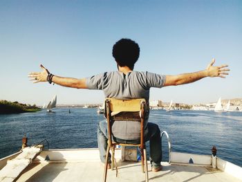 Rear view of man sitting by sea against clear sky