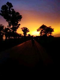 Silhouette trees by road against sky during sunset