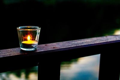 Illuminated tea light candle on railing at dusk