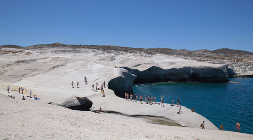 People on beach against clear blue sky