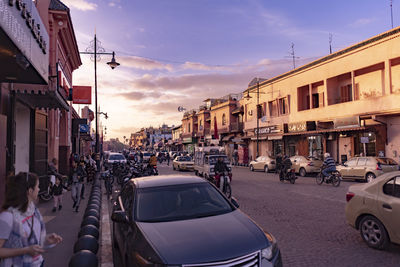 Vehicles on road along buildings at sunset