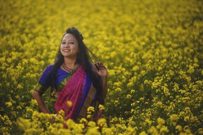 Portrait of woman standing amidst yellow flowering plants on field