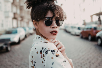 Portrait of young woman wearing sunglasses standing on street in city