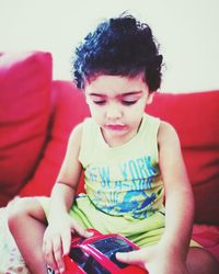 Close-up of boy sitting with toy car on sofa at home