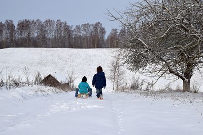 Rear view of siblings playing on snow covered field