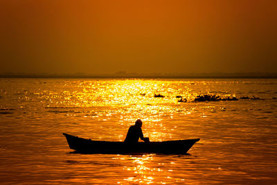 Silhouette man in sea against sky during sunset