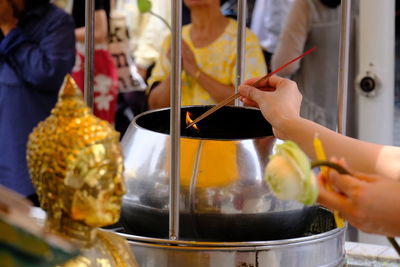 Midsection of woman burning incense sticks at buddha temple