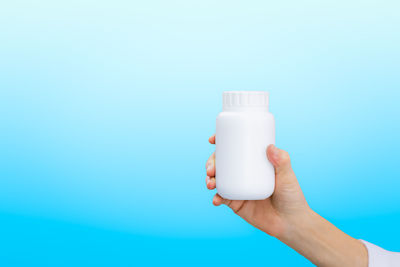 Cropped hand of woman holding bottle against white background