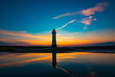 Lighthouse by sea against sky during sunset