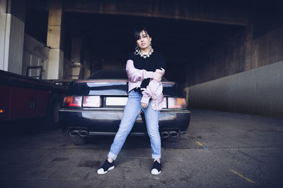 Portrait of young woman standing against car in parking lot