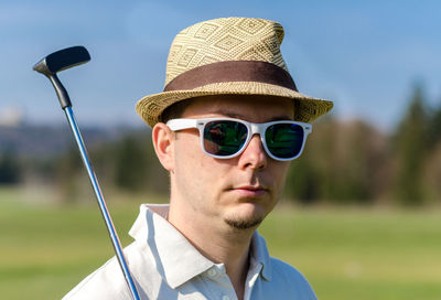 Portrait of man wearing sunglasses holding golf club standing on field