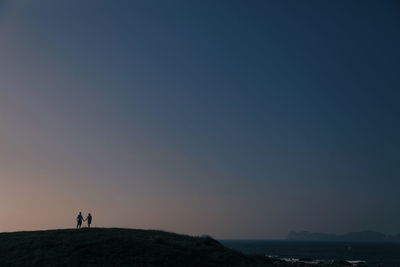 People standing on mountain by sea against clear sky