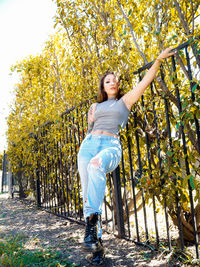 Portrait of young woman standing by railing and trees