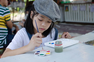 Close-up of girl with brush and watercolor paints sitting on table