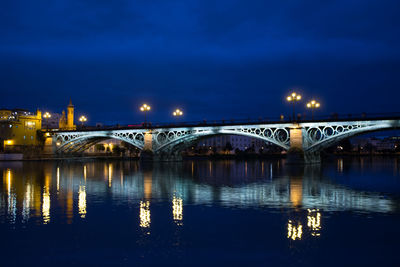 Illuminated bridge over river against sky at night