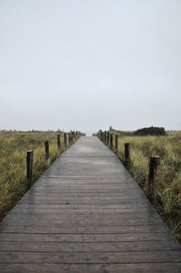 View of wooden footbridge on field against clear sky