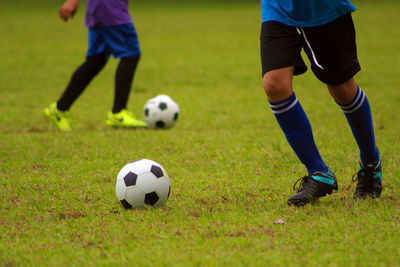 Low section of people playing soccer ball on grass