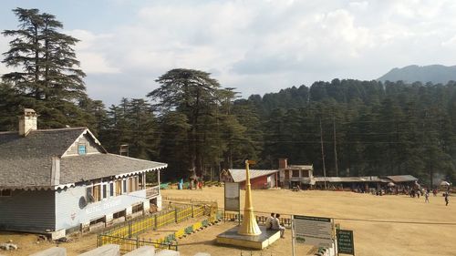 Built structure by trees and houses against sky