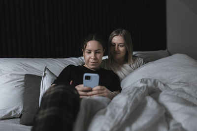 Female homosexual couple sitting in bed and looking at cell phone