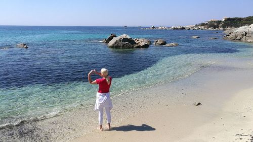 Rear view of woman making heart shape while standing at beach