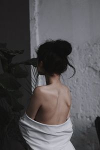 Rear view of shirtless woman standing against wall at home