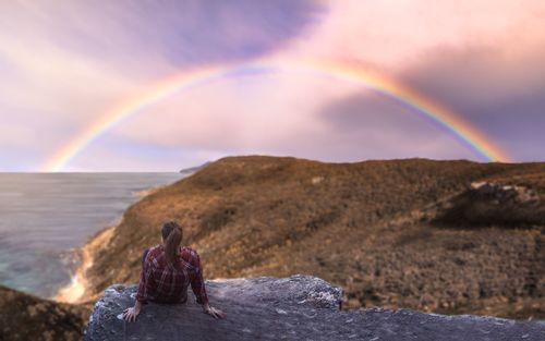 Rear view of woman on rainbow over mountain against sky