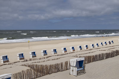 Hooded chairs on beach against sky