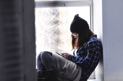 Young woman studying while sitting on window sill at home