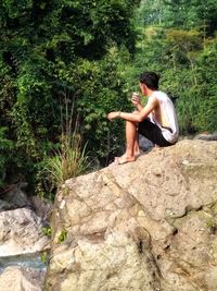 Side view of young woman sitting on rock in forest