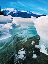 Low angle shot of a crack in the melting ice of frozen lake with mountains in the distance