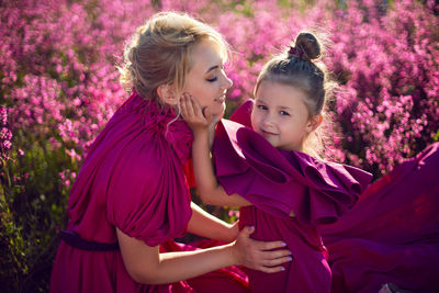 Happy family mother and daughter in pink dresses are sit in a field with flowers and big balloons 