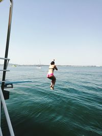 Full length rear view of woman jumping over sea against clear sky