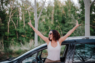 Woman standing in car against tree