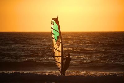 Silhouette man windsurfing on sea against clear sky during sunset