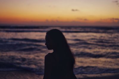 Silhouette young woman standing by sea against sky during sunset