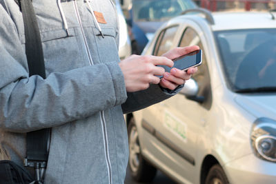 Midsection of man using mobile phone by cars on street