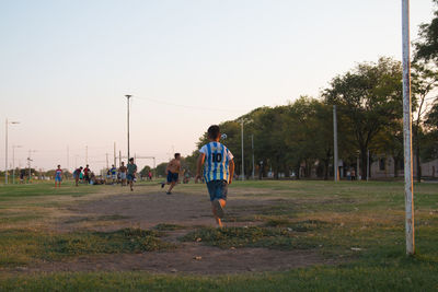 Rear view of people walking on field against clear sky