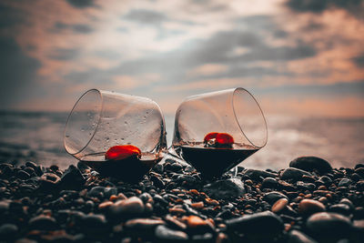 Close-up of wine glass on beach against sky during sunset