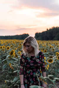 Woman amidst sunflowers on field against sky during sunset