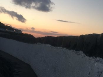 Snow covered landscape against sky during sunset