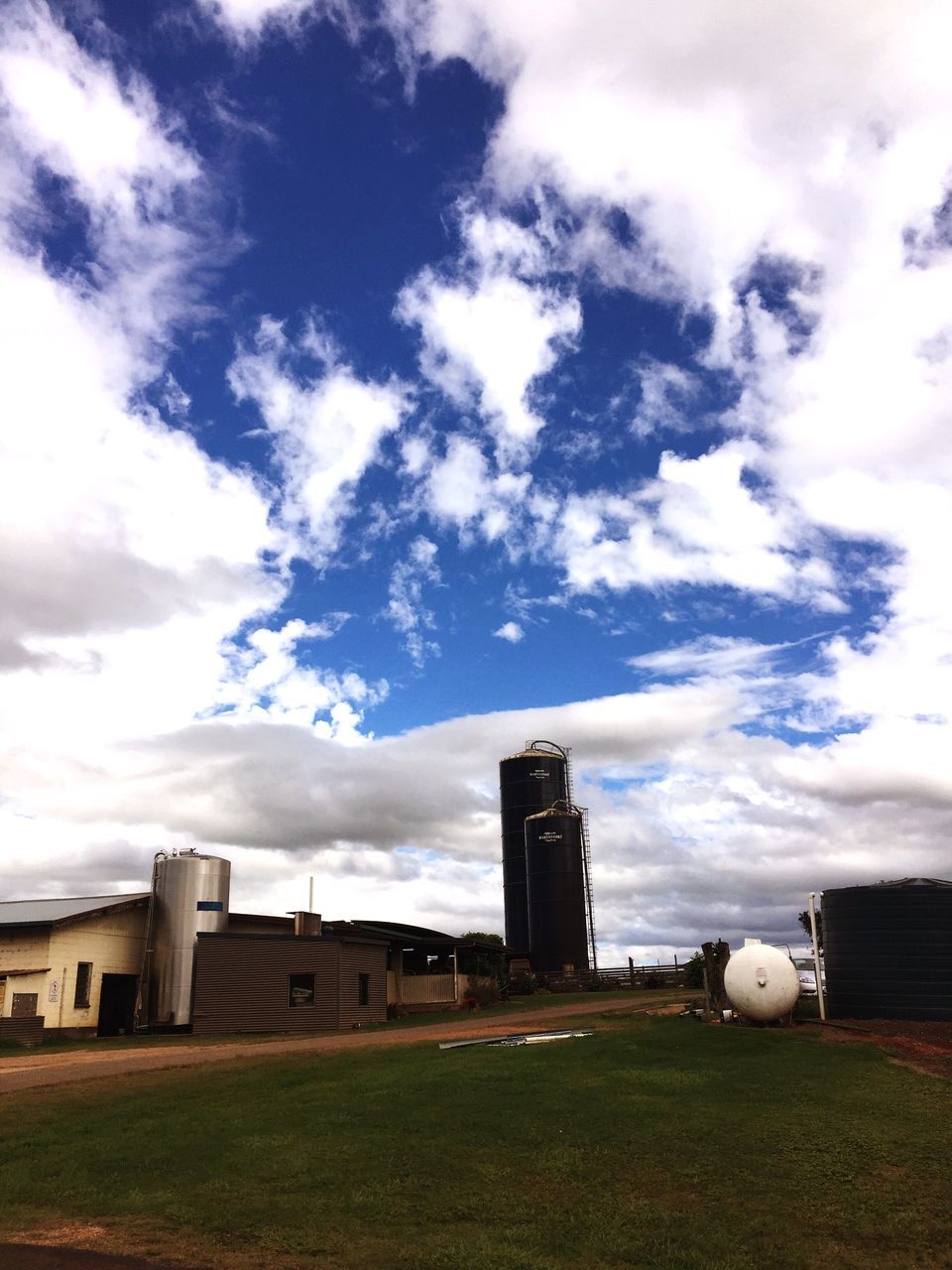 sky, architecture, built structure, cloud - sky, field, grass, cloudy, cloud, landscape, rural scene, grassy, no people, day, factory, outdoors, nature, overcast, weather, horizon over land, tranquility