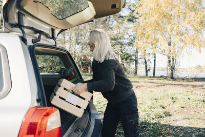 Side view of mature woman loading crate full of organic vegetables in car trunk